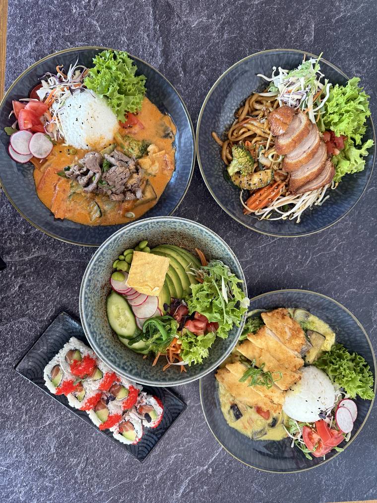 Auswahl aus Bowls, gebratenen Nudeln und Sushi auf einem Holztisch
