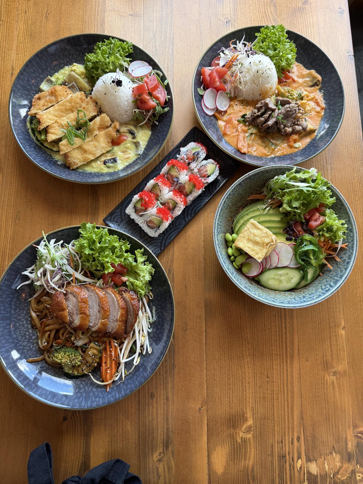 Gedeckter Tisch mit mehreren Bowls, einer Maki-Platte und Beilagen